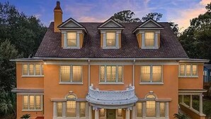Ein zweistöckiges Haus mit einer symmetrischen Fassade, einem zentralen Eingang mit einem überdachten Vorbau und einem Ziegelkamin.