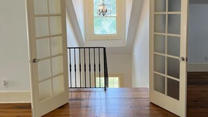 Ein geräumiges Zimmer mit Holzboden, einer weißen Tür mit Glasfeldern und einer Deckenleuchte.