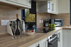 A modern kitchen with a wooden countertop, a microwave, a bowl of fruit, and two glasses of champagne. - High Range Holiday Apartments (Aviemore)