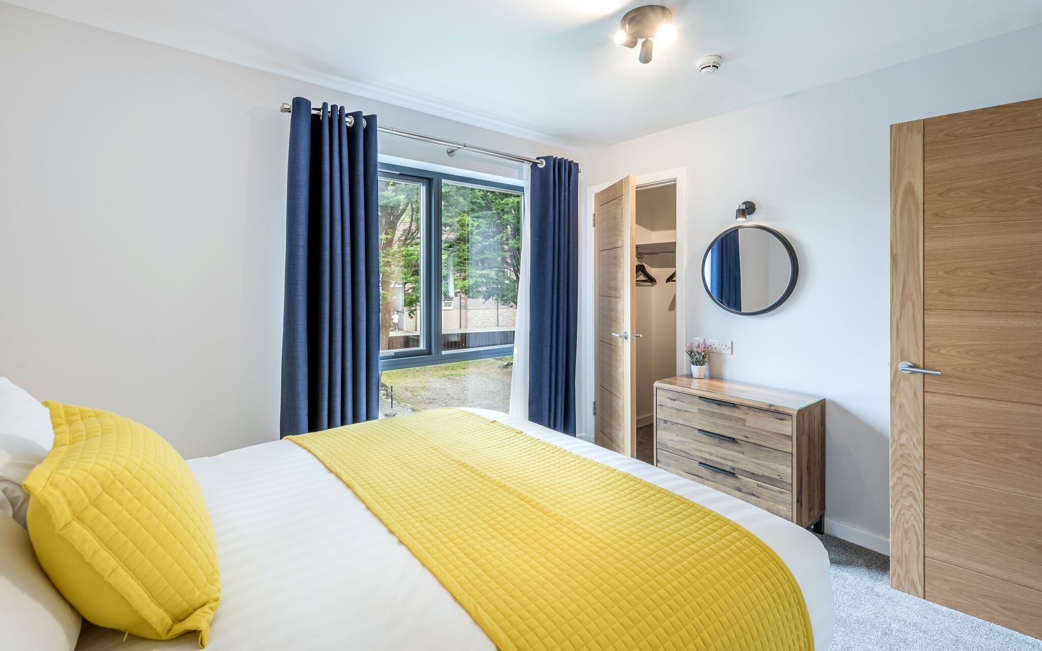 A bedroom with a bed, a dresser, a mirror, and a window with curtains.