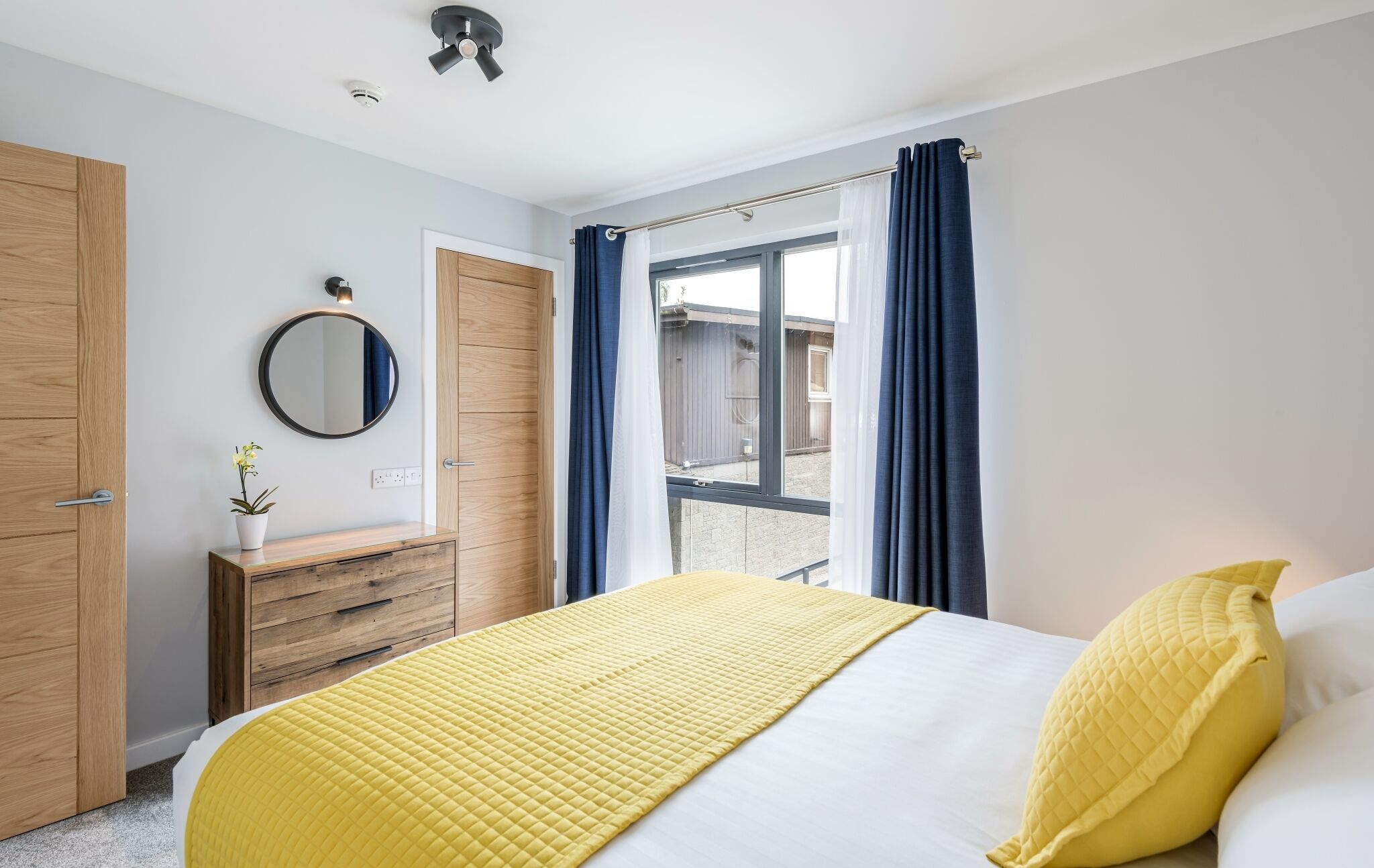 A bedroom with a bed, wooden wardrobe, a mirror, and a window with curtains.