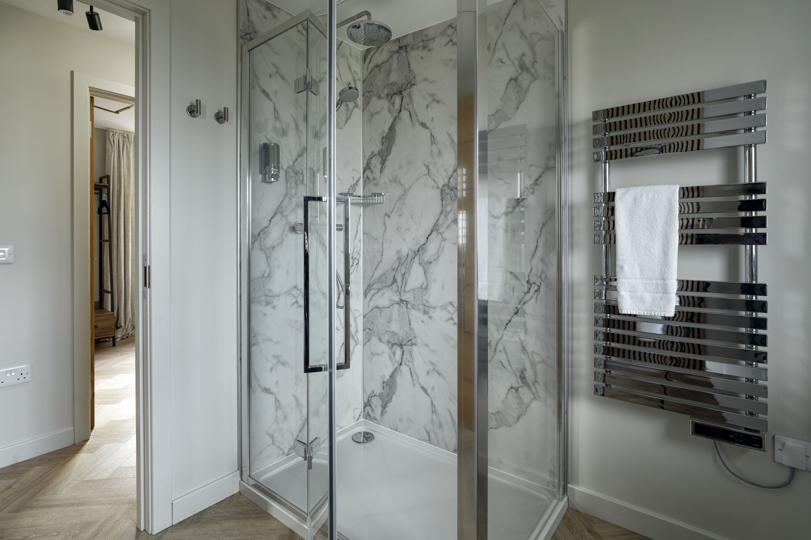 A modern bathroom with a glass-enclosed shower, marble walls, and a towel rack.