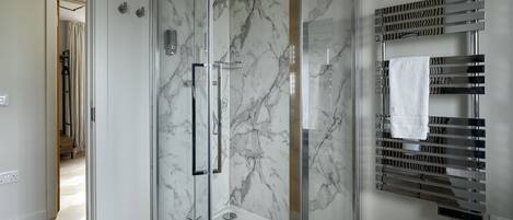 A modern bathroom with a glass-enclosed shower, marble walls, and a towel rack.