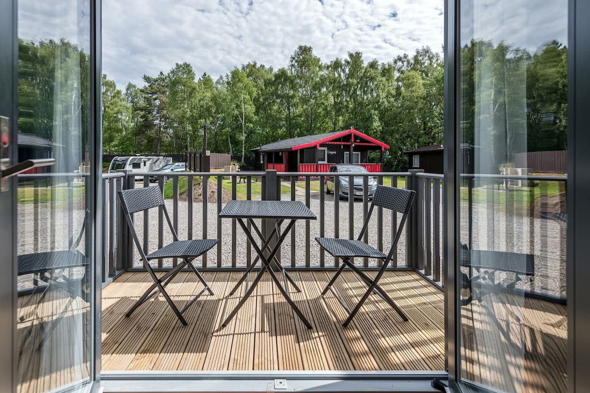 Un balcon doté d’une terrasse en bois, de deux chaises et d’une petite table.