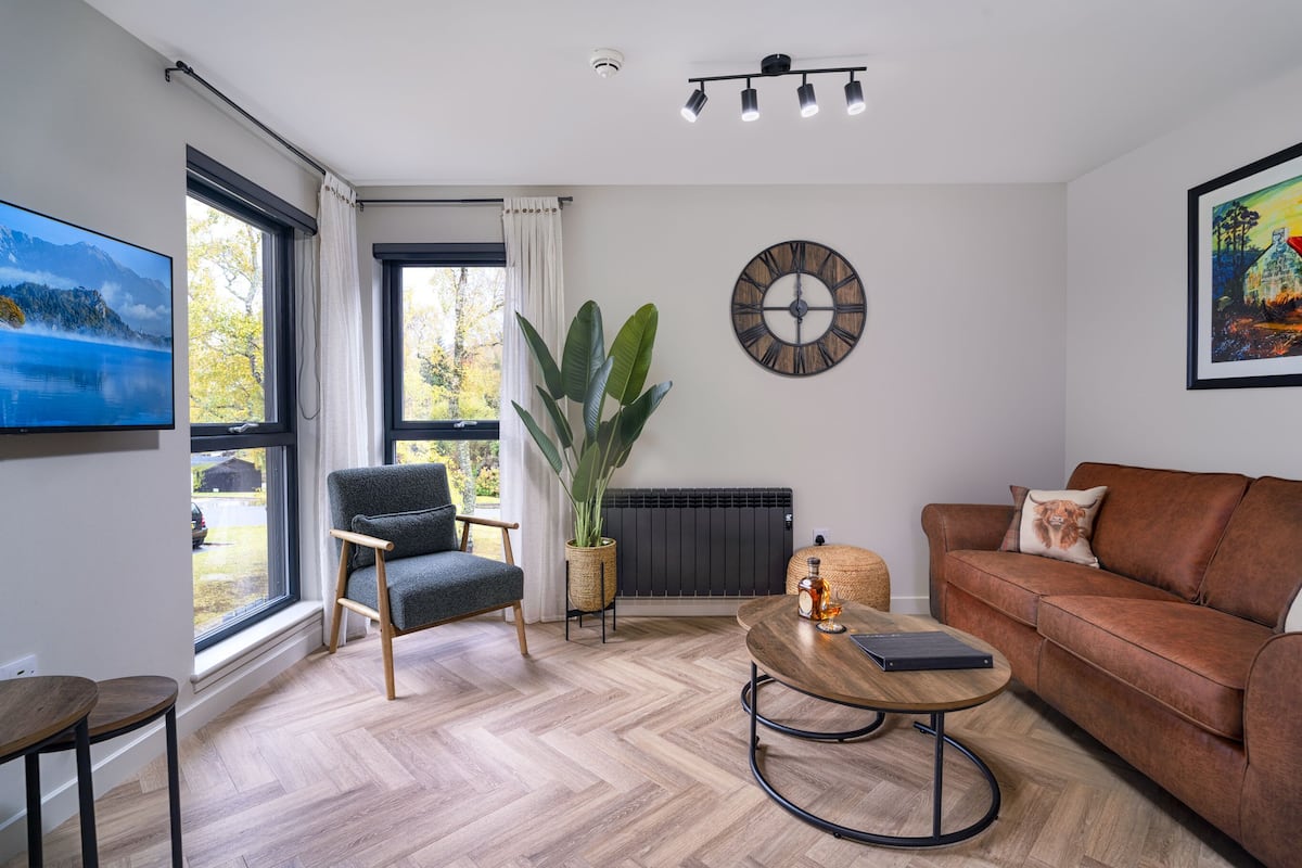 Un salon moderne avec une grande fenêtre, un canapé, une table basse et un téléviseur.