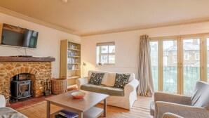 A cozy living room with a stone fireplace, a sofa with patterned cushions, a bookshelf, and a television mounted on the wall. - Stylish coastal living with sea views make this a great choice for your break. (Hunstanton)