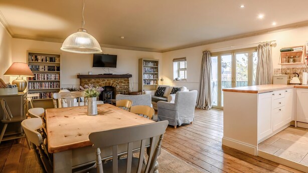 A cozy living room with a fireplace, a dining area with a wooden table and chairs, and a kitchen with white cabinets and a countertop. - Stylish coastal living with sea views make this a great choice for your break. (Hunstanton)