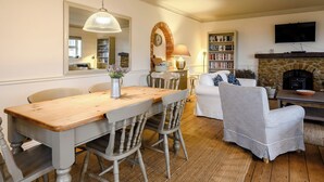 A cozy living room with a fireplace, a television mounted above it, and a bookshelf filled with books. - Stylish coastal living with sea views make this a great choice for your break. (Hunstanton)