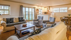 A cozy living room with a sofa, armchairs, and a coffee table. There is a kitchen area with cabinets and a window. - Stylish coastal living with sea views make this a great choice for your break. (Hunstanton)