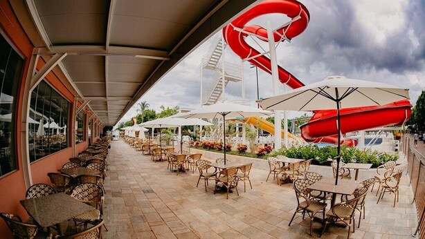 An outdoor patio with tables and chairs, a red water slide, and a covered walkway. - Diroma Fiori Hotel - BVTUR (Caldas Novas)