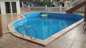 Ein Schwimmbad mit Steinplatten-Terrasse, einer weißen Brüstung und einer Treppe, die zu einer erhöhten Ebene führt.