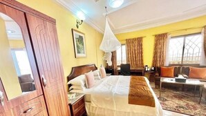 Ein Hotelzimmer mit einem großen Bett, einem Holzschrank, einem Schreibtisch, einem Stuhl, einer Couch und einem Fenster mit Vorhängen.