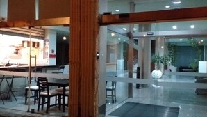 Moderni hotellin aula, jossa on lasiovet, vastaanottotiski sekä oleskelualue, jossa on tuoleja ja pöytiä.