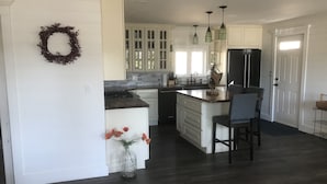 Een moderne keuken met witte kasten, een centraal eiland en een eethoek met een stoel.