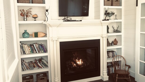 Een woonkamer met een open haard, een wandtelevisie en boekenkasten vol boeken.