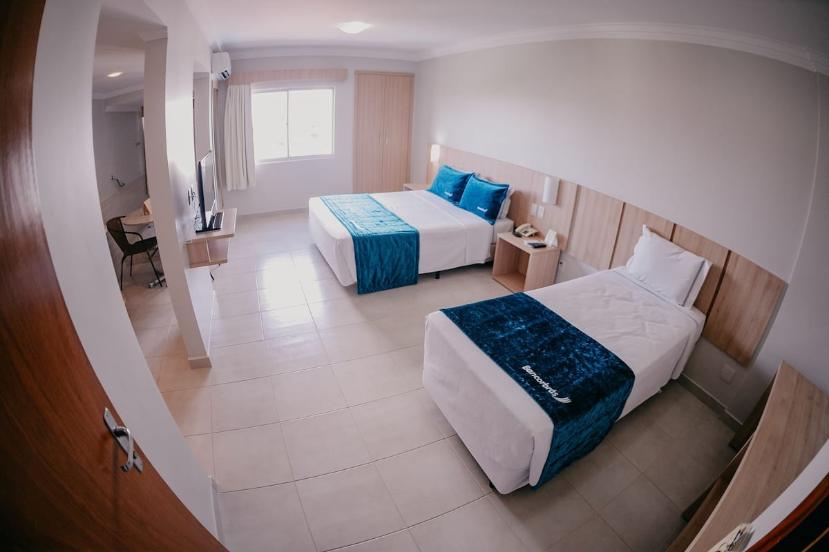 Quarto de hotel com duas camas, uma escrivaninha e área de chuveiro.