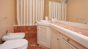 A bathroom with a bathtub, two toilets, a sink, and a mirror.