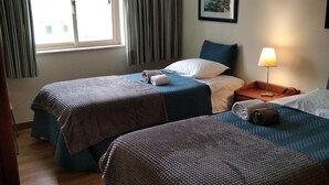 Habitación de hotel con dos camas, una ventana con cortinas, una lámpara de noche y un cuadro en la pared.
