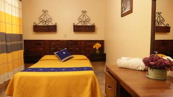 Habitación de hotel con cama, cabecera de madera, mesita de noche con un florero, espejo y estante en la pared.