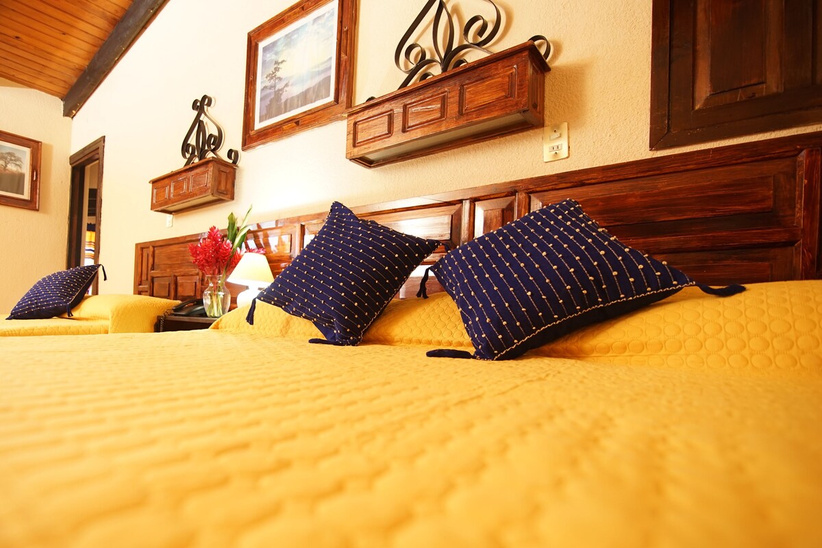 Ein Hotelzimmer mit zwei Betten, Holz-Kopfteilen und einer Holzbalkendecke.