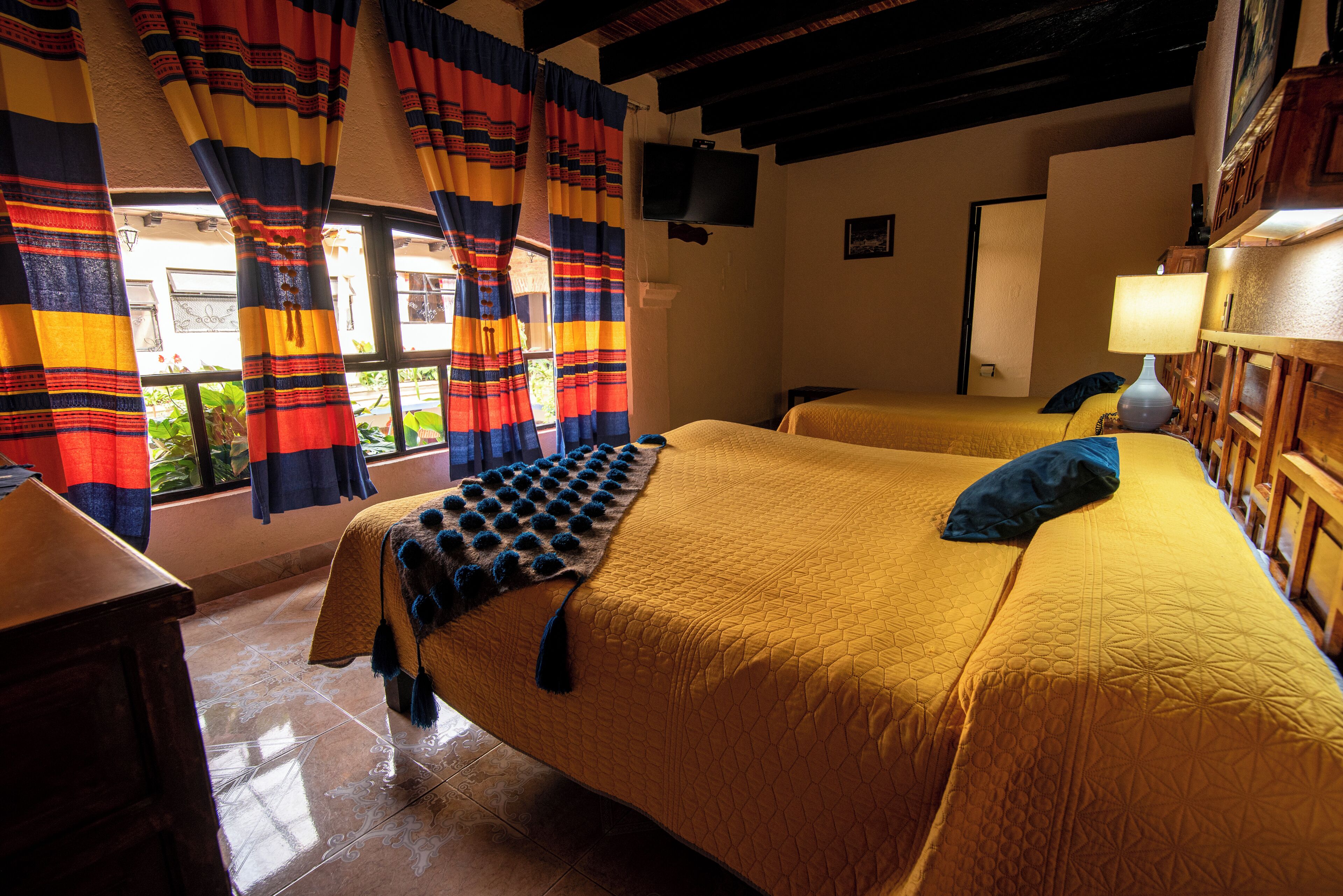 A hotel room with two beds, a television, and a window with curtains.