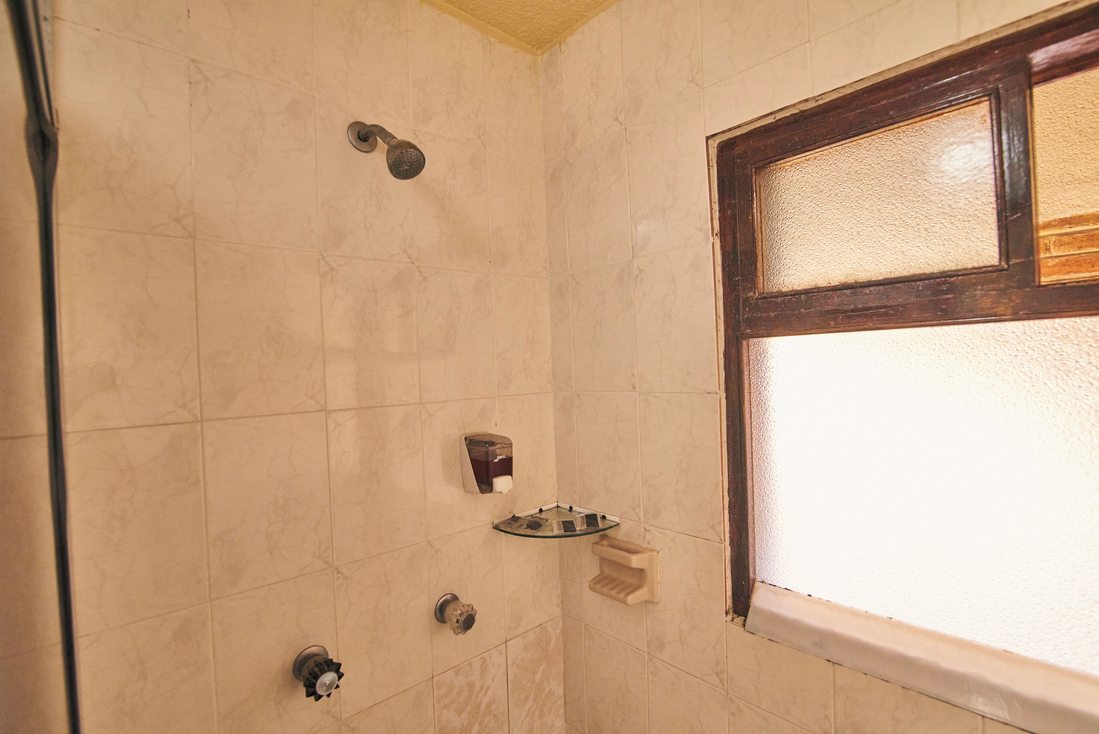 A bathroom with a shower, a hand soap dispenser, and a window.