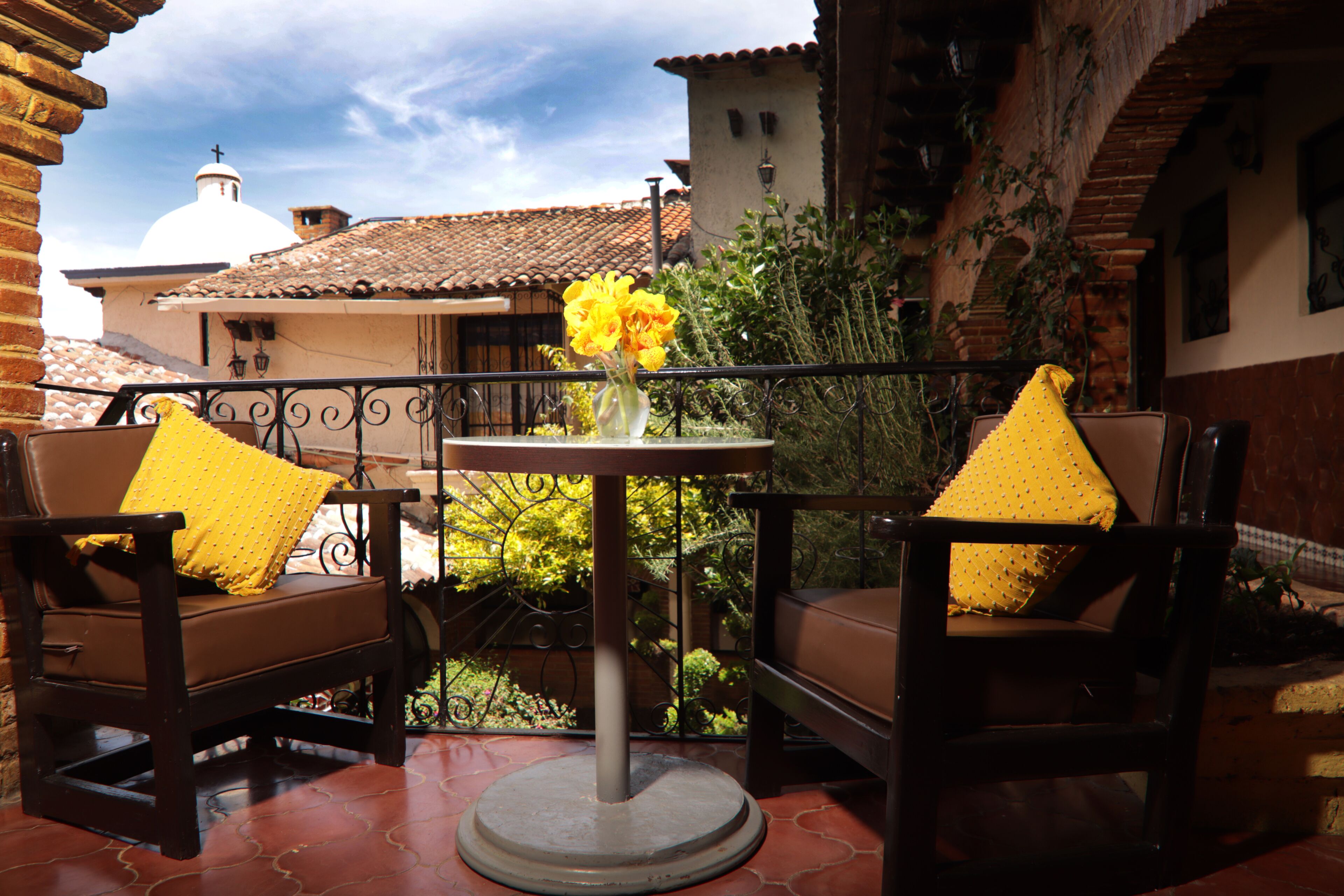 A patio with two brown leather chairs, each with a yellow pillow, and a small round table with a vase of yellow flowers.
