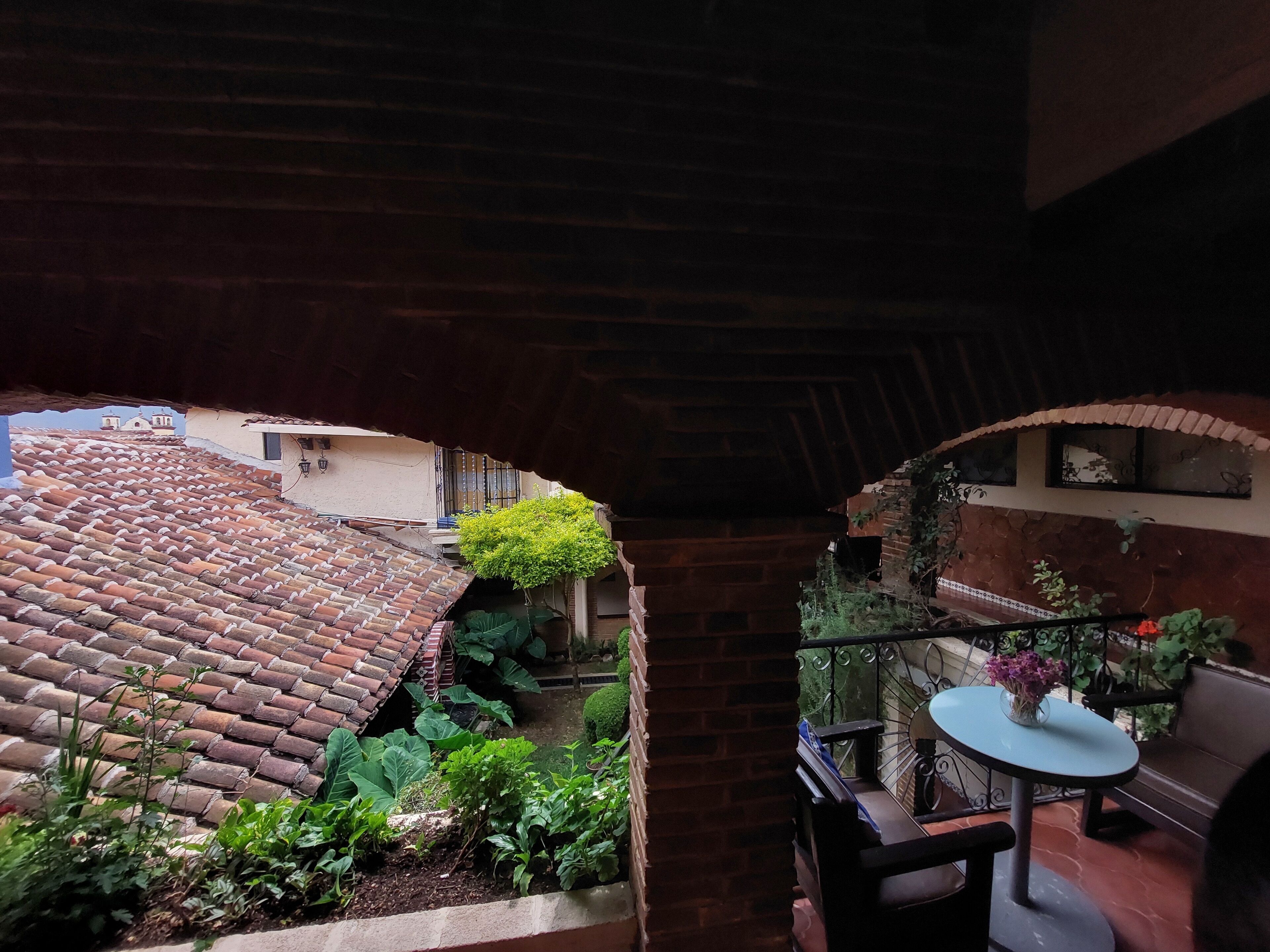 A rooftop garden with terracotta tiles, a small table with a vase, and a brick wall with a window.