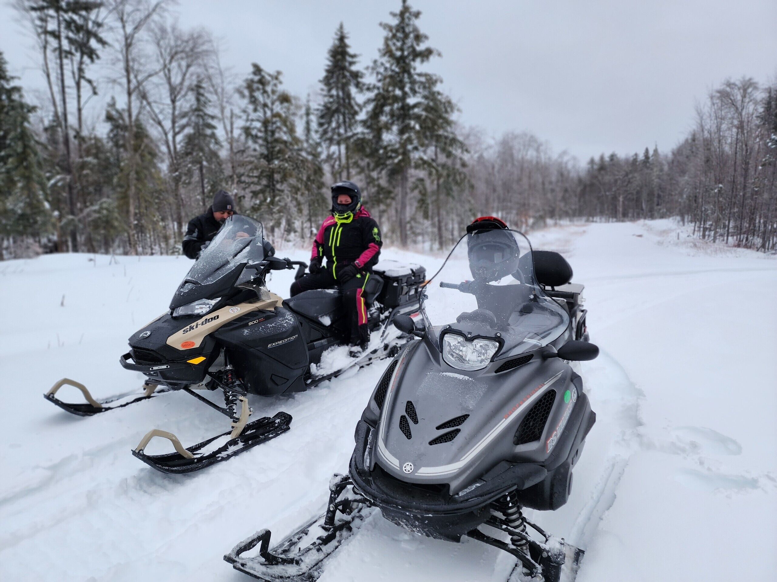 Two snowmobiles on a snowy path with trees in the background.