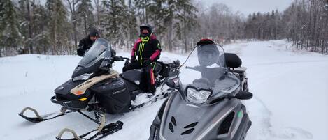 Two snowmobiles on a snowy path with trees in the background.