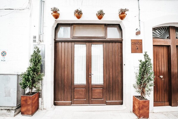 A building with a large wooden double door, a sign with the number 5, and two potted plants on either side of the entrance.