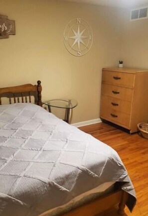 A bedroom with a wooden bed, a small bedside table, a dresser, and a compass wall decoration.