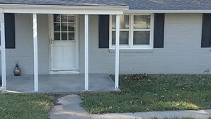 Una casa de un piso con un porche delantero, una puerta blanca y una ventana con contraventanas.