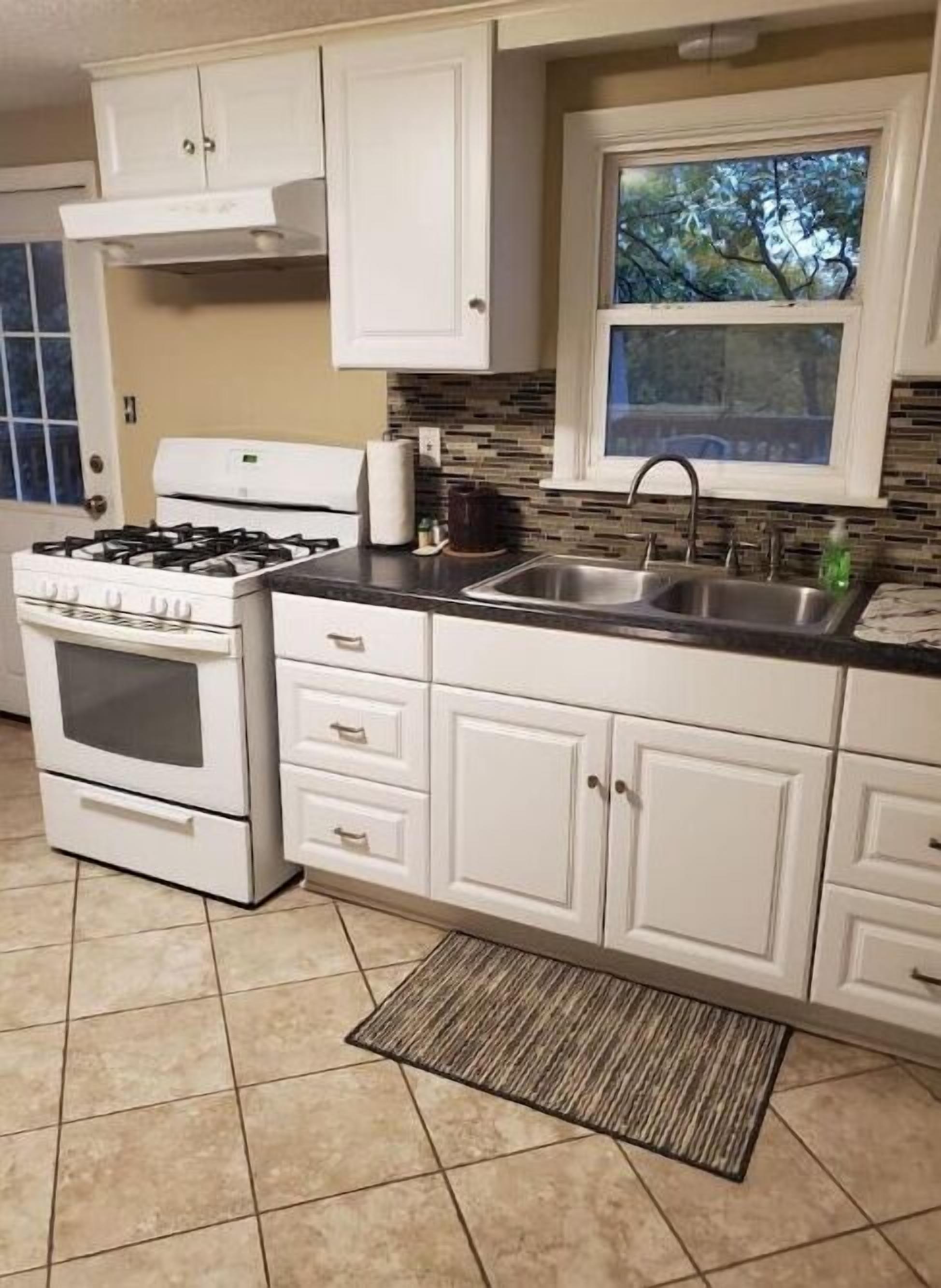 A kitchen with white cabinets, a gas stove, a sink, and a window with a view of trees.