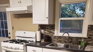 Una cocina con gabinetes blancos, una estufa a gas, un lavamanos y una ventana con vista a árboles.
