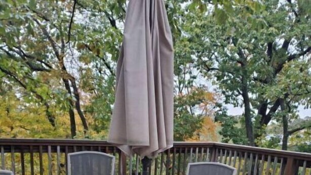 Un porche techado al aire libre con una mesa y sillas, rodeado por una terraza de madera y árboles.