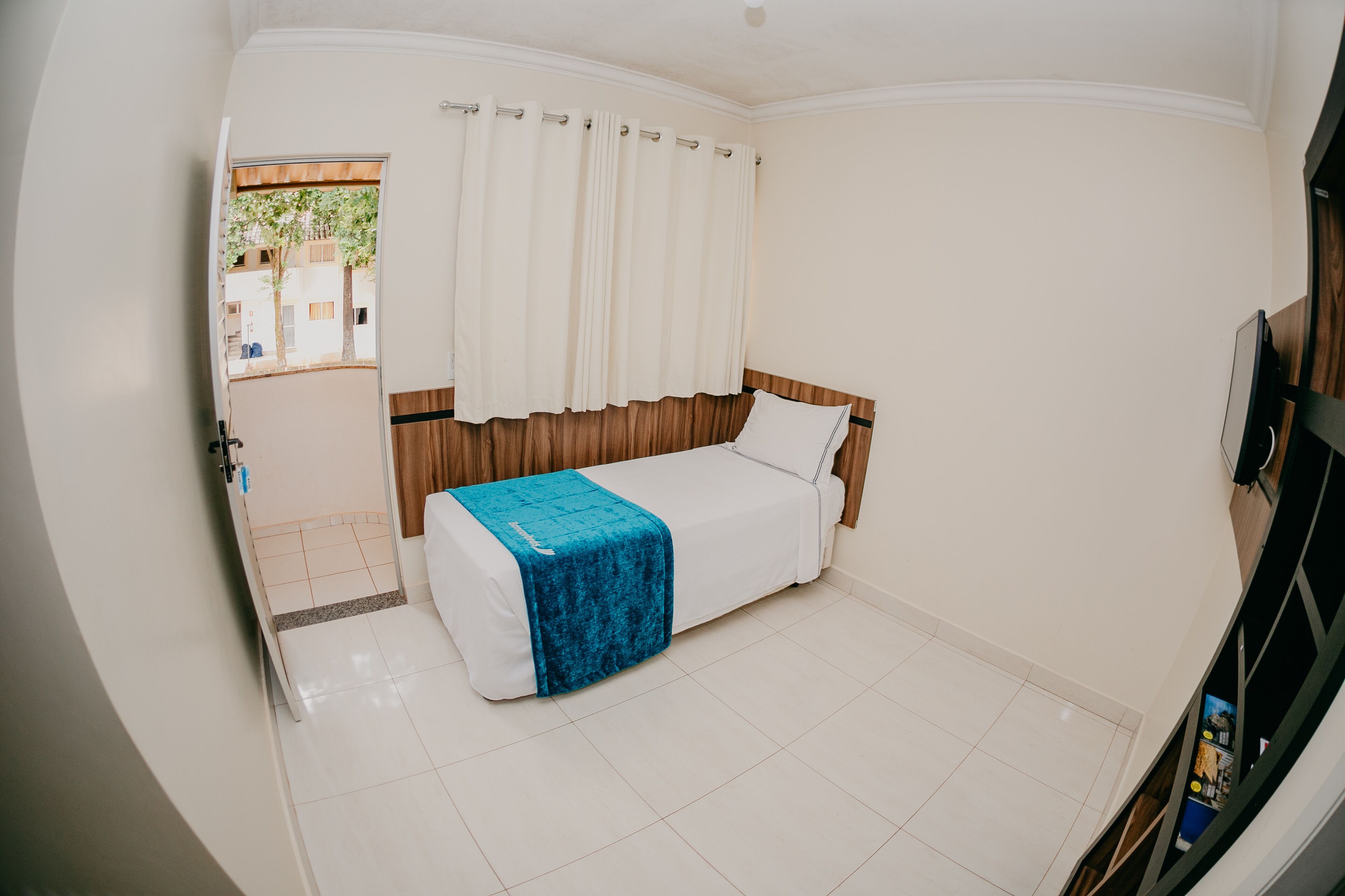 A hotel room with a bed, a window with curtains, a wooden headboard, and a tiled floor.