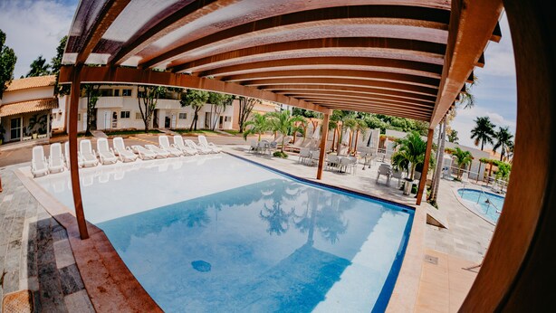 A swimming pool with lounge chairs and a covered area. - Diroma Internacional Resort - BVTUR (Caldas Novas)