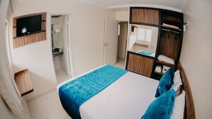 A bedroom with a bed, a TV mounted on the wall, a wardrobe, and a bathroom visible through an open door. - Diroma Internacional Resort - BVTUR (Caldas Novas)