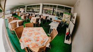 A restaurant with wicker tables and chairs, a green carpet, and a view of the outdoors through large windows. - Diroma Internacional Resort - BVTUR (Caldas Novas)