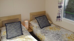 Een kamer met twee enkele bedden, elk voorzien van een hoofdeinde, een bedlampje en een raam met gordijnen.