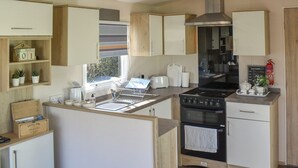 Een compacte keuken met een kookplaat, oven en spoelbak, houten kastjes en een raam met uitzicht.