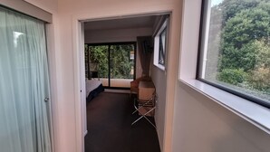 Ein schmaler Flur mit einer Schiebetür zur linken Seite, die auf einen Balkon mit Blick auf Bäume führt. Rechts ist ein Karton und ein Metallgestell zu sehen.