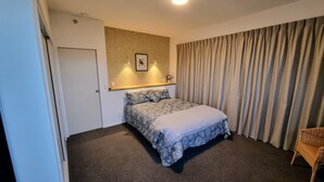 Ein Schlafzimmer mit einem Bett, einem Sessel, einem an der Wand befestigten Regal mit einer Vase und einem Vorhang.