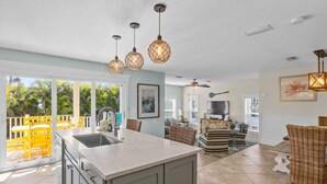 A spacious kitchen with a large island, a dining area with yellow chairs, and a living room with wicker furniture. - Ocean Walk- 5 bedroom heated pool/spa and 6 houses from the white sandy beach (Anna Maria)