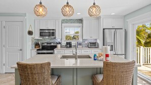 A modern kitchen with white cabinets, a central island with wicker chairs, and hanging pendant lights. - Ocean Walk- 5 bedroom heated pool/spa and 6 houses from the white sandy beach (Anna Maria)