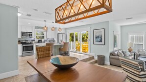 A modern kitchen with white cabinets, a large island, and a dining area with a wooden table and chairs. - Ocean Walk- 5 bedroom heated pool/spa and 6 houses from the white sandy beach (Anna Maria)