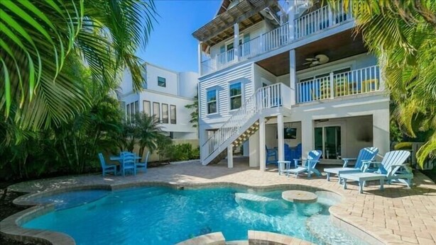 A two-story building with a swimming pool, outdoor seating, and a staircase leading to the upper floor. - Ocean Walk- 5 bedroom heated pool/spa and 6 houses from the white sandy beach (Anna Maria)