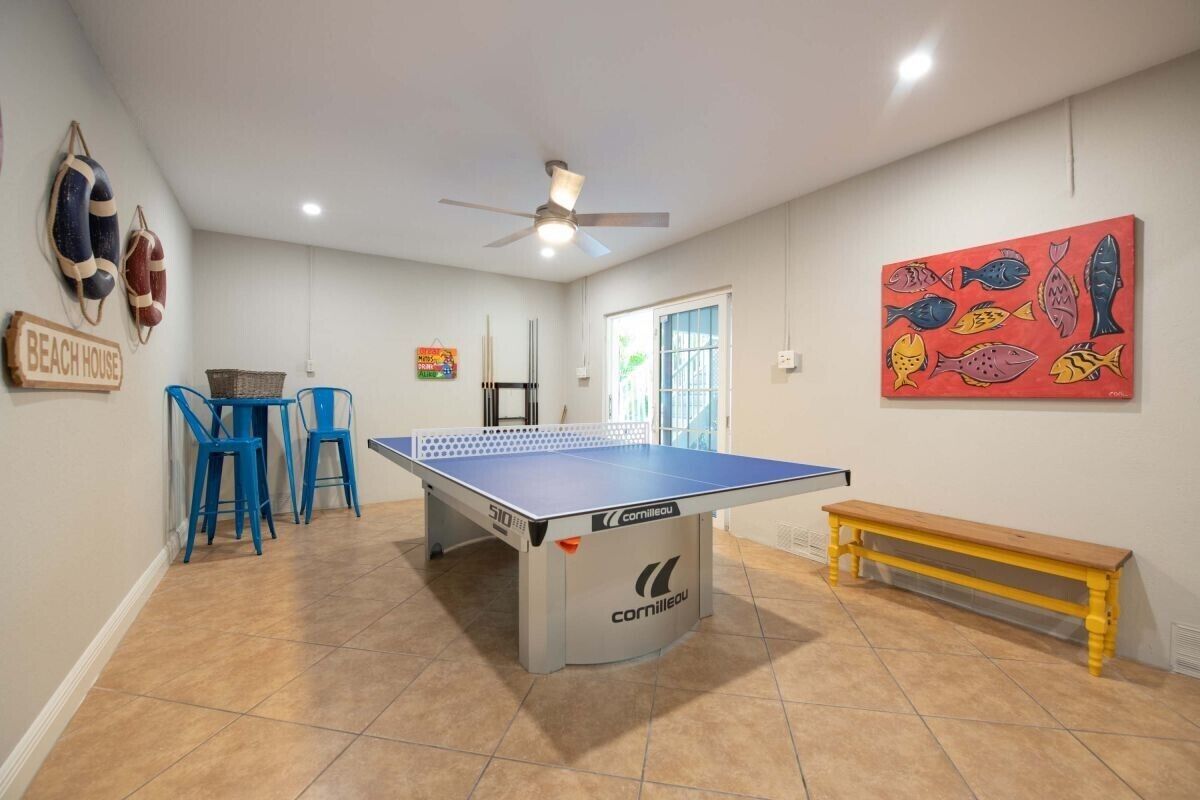 A room with a ping pong table, blue chairs, a wooden bench, and a painting of fish on the wall.