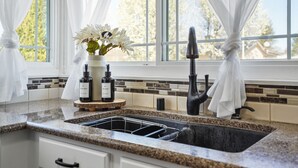 A kitchen with a granite countertop, a stainless steel sink, and a window with white curtains.